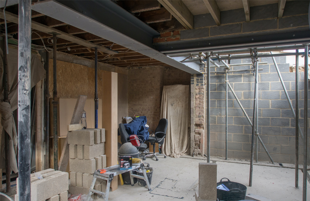 Innenansicht einer Baustelle mit Baumaterialien, Gerüsten und Werkzeugen, vorbereitet für umfassende Sanierungsarbeiten an einer Immobilie.