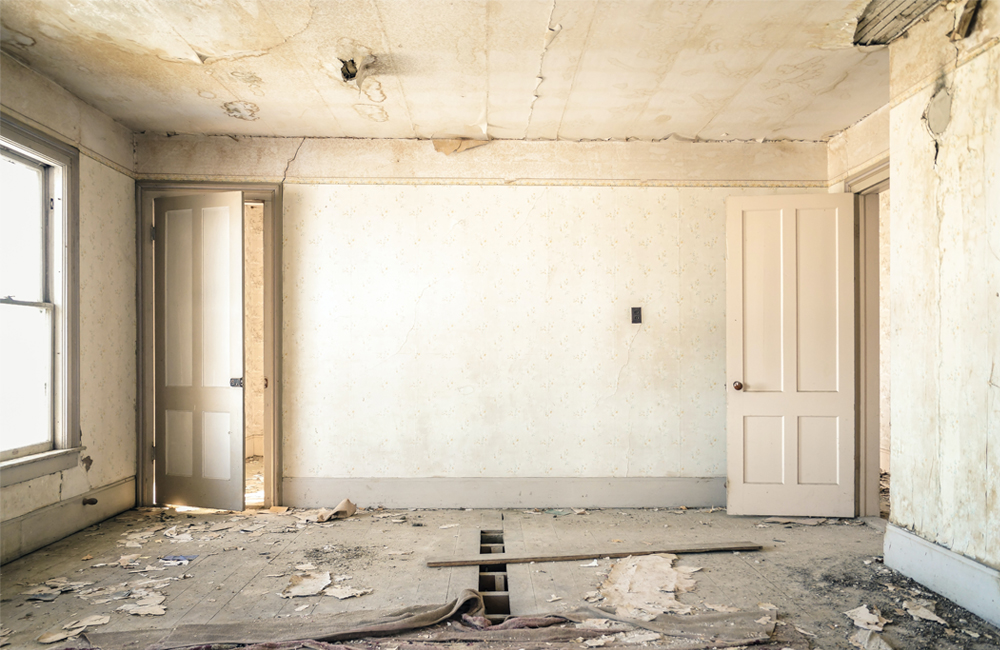 Sanierungsbedürftiger Raum mit beschädigter Decke, abblätternder Tapete und unebenem Holzboden, bereit für eine Komplettsanierung.